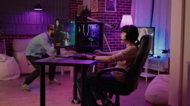 Gamer girl celebrating victory in action space simulation game while boyfriend is playing virtual reality first person shooter at home. Couple in online gaming competition using pc and vr goggles.