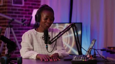 Afrika asıllı Amerikalı kadın podcaster 'ın portresi masa başında oturmuş ev kayıt stüdyosundaki dizüstü bilgisayardan içeriği okuyor. Seyirciler için canlı yayın yaparken kendine güvenen bir radyo sunucusu..