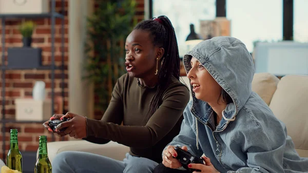 Multiethnic team of women playing video games online on television console, having fun with gaming competition. Cheerful people using controller to play challenge together. Handheld shot.