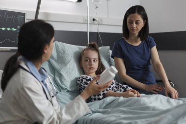 Doctor expert recommending antibiotics for ill kid sickness hospitalized in children healthcare facility. Expert pediatrician prescribing medication for little girl disease resting in patient bed.