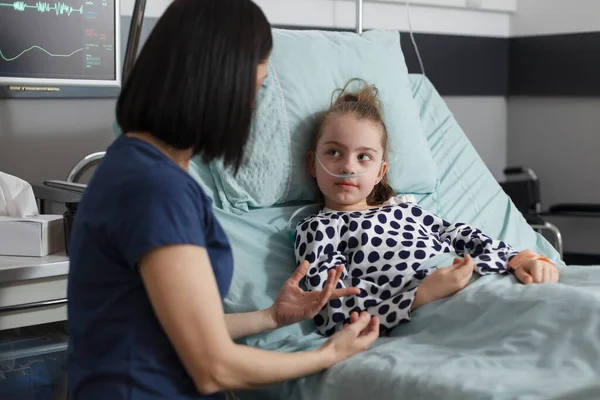 入院中の病気の娘と話をする母を介護しながら治療中の小児病棟患者のベッドで休んでいます 彼女を慰めながら 親は病気の女の子の横に座って思いやり — ストック写真