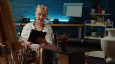 Wheelchair user with health condition using tablet to find inspiration on internet to draw masterpiece. Drawing artwork sketch with pencils and dealing with chronic impairment.