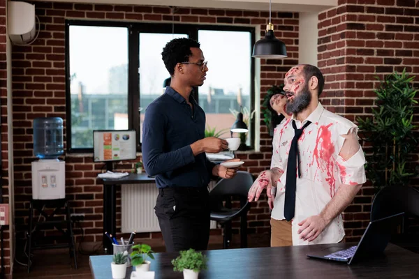 African american man talking to zombie in business office, undead spooky corpse chatting with person in startup workplace. Evil horror macabre monster with bloody scars and decayed.