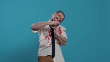Korkunç kötü görünümlü zombi mavi arka planda el hareketi yapıyor. Korkunç, beyinsiz, vahiysel canavar kameraya bakarken mola zamanı el sinyali veriyor. Stüdyo çekimi