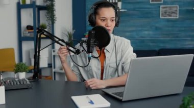 Famous internet space influencer sitting at home studio desk while filming vlog. Creative social media content creator hosting show in living room while having modern audio equipment.