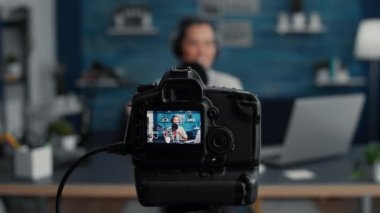 Professional modern camera recording internet star talking to audience. Popular social media content creator filming vlog for video sharing platforms while sitting at studio desk. Close up
