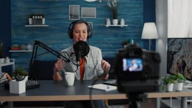 Famous internet influencer greeting audience while starting to record podcast. Young attractive social media star filming herself talking with public while sitting at home studio desk.