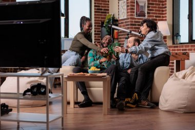 Bir grup insan bira şişelerini tokuşturuyor ve tezahürat yapıyor. Ev partisinde arkadaşlarıyla buluşmalarını kutluyorlar. Erkekler ve kadınlar alkollü içeceklerle kadeh kaldırıyor, birlikte eğleniyorlar..