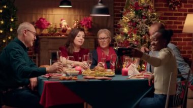 Neşeli aile üyeleri, Noel yemeği masasında otururken akıllı telefon cihazıyla selfie çekiyorlar. Şenlikli çeşitli insanlar, Noel tatilini Xmas 'ın dekore edilmiş dairesinde birlikte kutluyor..