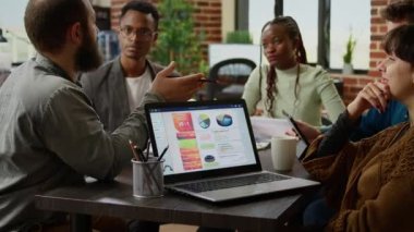 Diverse team of colleagues doing collaboration work with charts and graphs, using documents to do project research. People attending business meeting in company boardroom, teamwork.