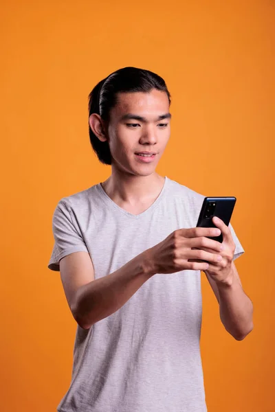 Young asian man typing message on smartphone, online communication concept. Cheerful teenager standing, browsing internet on mobile phone, attractive person using social media