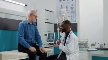 Medic physician explaining x ray scan results to patient in medical cabinet, analyzing bones radiography diagnosis on digital tablet to give treatment. Healthcare checkup appointment with doctor.
