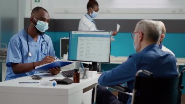 Erkek hemşire, covid 19 salgını sırasında yaşlı bir hastayla görüşüyor. Kronik bozukluğu olan bir adamla ve eşiyle konuşuyor. Uzman, felçli birine check-up yapıyor..