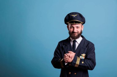 Profesyonel üniformalı heyecanlı bir uçak pilotu el çırpıyor. Mutlu olumlu uçak pilotları alkışlıyor, avuç içlerini sallıyor, ayakta duruyor, kameraya bakıyor, stüdyo orta çekimde.