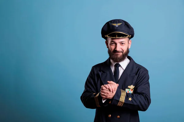 Smiling excited plane aviator in professional uniform clapping hands. Happy positive airlane pilot applauding, shaking palms, standing, looking at camera, studio medium shot