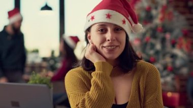 Noel Baba şapkalı genç bir kadının portresi ofis odasında dizüstü bilgisayarla çalışıyor Noel ağacı ve süslemelerle dolu. Kış bayramı şenliği sırasında masa başında çalışmak için oturan kişi.