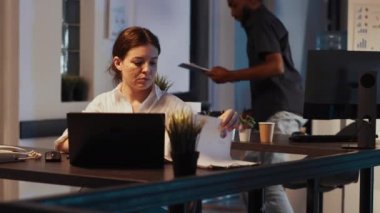 Genç yetişkin uzaktan konuşmak için sabit telefonu kullanıyor, başlangıç veri araştırmaları ile rapor ve sunum planlamak için çalışıyor. Küçük işletme ofisinde gelir paylaşımı planlama.
