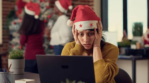 疲惫不堪的女人带着圣诞装饰品和装饰品试图在嘈杂的办公室里工作 压力很大的人在工作时被快乐的人们庆祝圣诞节和寒假打断了 — 图库照片