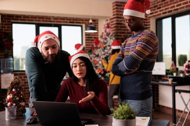 Noel arifesinde çalışan bir grup insan, Xmas ışıkları ve şenlikli dekorasyonlarla ofis projelerini planlamak için takım çalışması yapıyor. İşte dizüstü bilgisayar kullanmak, mevsimlik kış tatili..