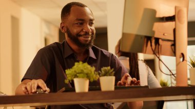 Company employee analyzing online report data to create business project, working on web presentation with network information on computer. Working during sunset. Handheld shot.