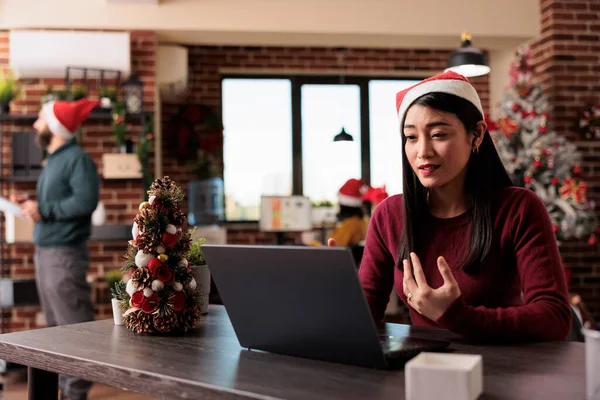 Businesswoman attending videocall meeting in office decorated with christmas tree. Talking on online remote videoconference and teleconference call in workplace with holiday ornaments.