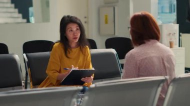 Asyalı kadınlar tesis lobisinde tıbbi raporlardan bahsediyorlar. Doktorla muayene randevusuna gitmeden önce check-up formu dolduruyorlar. Hastane kliniğinde bekleme odasında oturuyor..