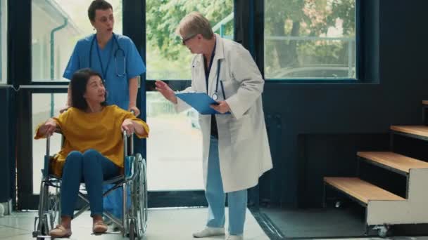 帮助轮椅受损病人的医疗助理 到保健中心看病 大厅中患有慢性身体残疾的女轮椅使用者 — 图库视频影像