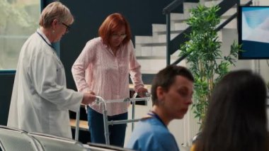 Yaşlı doktor bacak kırığı olan bir kadına iyileşmesi için yardım ediyor. Rehabilitasyon fizyoterapisinde yürüyen çerçeve kullanıyor. Fiziksel travması olan yaralı hastaya destek veriyor..