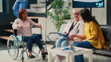 Asyalı kadınlar tesis lobisinde doktorla check-up yapıyor, kronik engelli ve fiziksel özürlü bir doktora danışıyorlar. Tekerlekli sandalye kullanıcılarına rehabilitasyon desteği.