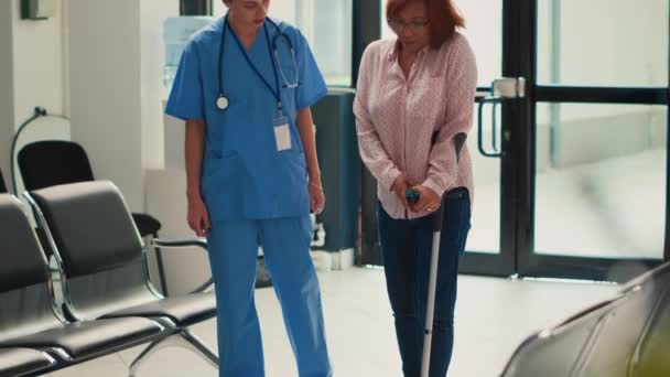 杖で歩く障害のあるアジアの女性 看護師はサポートを提供し 障害のある人を助ける 患者は事故後に足を回復しようとします 物理的な骨折を持っています 手持ち撮影 — ストック動画