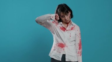 Kötü kalpli, beyin ölümü gerçekleşmiş zombi mavi arka planda dururken el işareti yapıyor. Onaylamayan çılgın görünümlü kötü canavar kameraya bakarken el hareketi yapıyor..
