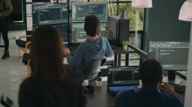 Sistem mühendisi birden fazla monitörün kodunu kontrol ediyor ve ajans ofisinde uygulama geliştiricisi meslektaşıyla çalışıyor. Ekranlardaki algoritmayı analiz eden kodlayıcı, yeni kullanıcı arayüzü geliştiriyor.