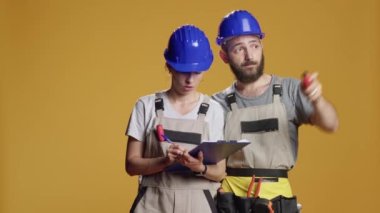 İnşaat işçileri kâğıtların ölçüsünü hesaplıyor, notlar alıyor ve inşa sürecini planlıyorlar. Yenileme ve yenileme ve endüstriyel onarım üzerinde çalışmak için kask ve tulum giyiyorlar..