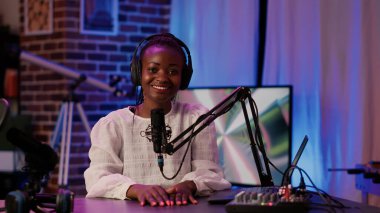 Afrika asıllı Amerikalı kadın podcaster 'ın portresi masa başında oturmuş ev kayıt stüdyosundaki dizüstü bilgisayardan içeriği okuyor. Seyirciler için canlı yayın yaparken kendine güvenen bir radyo sunucusu..