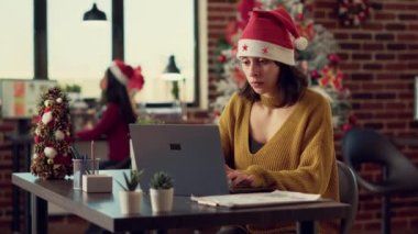Ofis çalışanı kış şenliği sırasında bilgisayarı kullanarak dizüstü bilgisayarda proje başlatmayı planlıyor. Uzayda, mevsimlik dekorasyonlar ve Noel ağacıyla çalışan neşeli kadın..