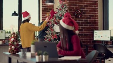 Çeşitli meslektaşlar Noel ağacına süsler takıyor, kış tatilini iş yerinde kutluyorlar. Ofisi xmas ışıkları ve şenlikli süslemelerle süslemek, mevsimlik dekorlardan mutlu olmak..