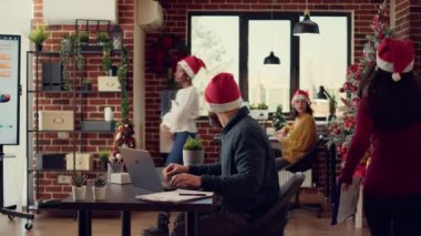 Bir grup meslektaşım Noel arifesinde festival ofisinde dizüstü bilgisayarla rapor inceliyor. Noel Baba şapkalı bir adam ve kadın, mevsimlik Noel ağacı dekoruyla uzayda takım çalışması yapıyorlar..
