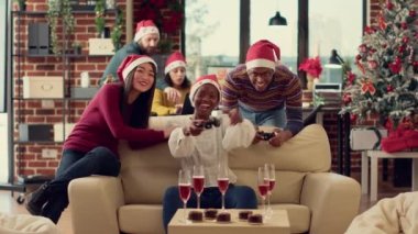 Neşeli insanlar kış tatili partisinde çevrimiçi video oyunlarıyla eğleniyorlar, Noel arifesini ofiste kutluyorlar ve konsolda oynuyorlar. Xmas festivalinde yarışmayla eğleniyorum. Üçayak atışı.