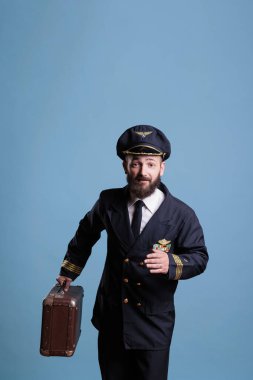 Profesyonel havayolu üniformalı bir uçak pilotu uçuşa geç kalıyor, yanında antika bavul taşıyor, önden bakıyor. Bavullu pilot havaalanında yürüyor, havacı bavulu tutuyor, kameraya bakıyor.