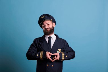 Mutlu uçak kaptanı kalp şeklindeki aşk sembolünü parmaklarıyla gösteriyor, kavramsal romantizm jesti. Üniformalı, dost canlısı bir uçak pilotu. Şefkat duyguları ifade ediyor.