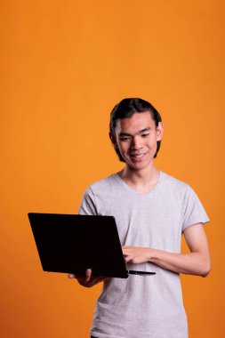 Bilgisayarda çalışan genç bir işçi, online eğitim programı izleyen bir öğrenci, evdeki internet kurslarına katılıyor. Gülümseyen Asyalı serbest yazar taşınabilir bilgisayar tutuyor.