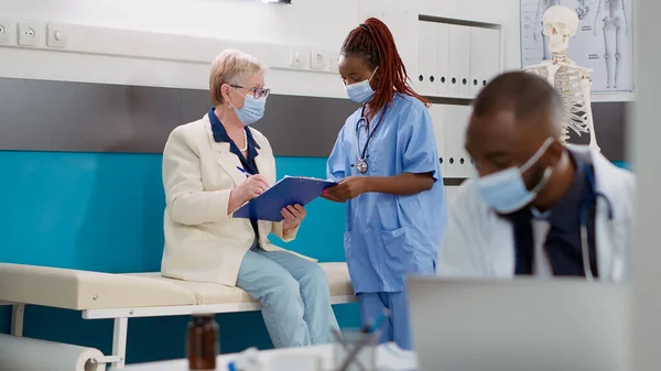 Medical Assistant Consulting Old Woman Covid Pandemic Cabinet Doing Checkup — стоковое фото