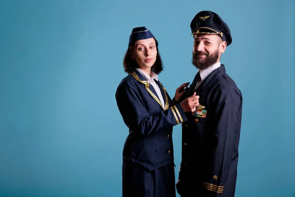 Smiling airplane pilot and flight attendant couple in uniform looking at camera, studio medium shot portrait. Airplane crew, plane captain and air hostess standing, aircrew