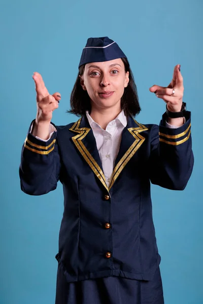 Smiling flight attendant showing emergency exit on plane board, safety instruction demonstration. Stewardess in professional uniform pointing with fingers at camera front view