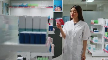 Eczane raflarındaki ilaç ürünlerini inceleyen neşeli Asyalı işçiler ilaç kutularına ve ilaç şişelerine bakıyorlar. Kadın eczacı vitamin ve uyuşturucu paketlerini kontrol ediyor..