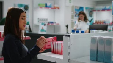 Eczane tezgahından sağlık ilacı almak için kardiyoloji hapları taşıyan Asyalı bir müşteri eczacıyla destek ve tedavi hakkında konuşuyor. Uyuşturucu ve eczacılara bakıyorum..