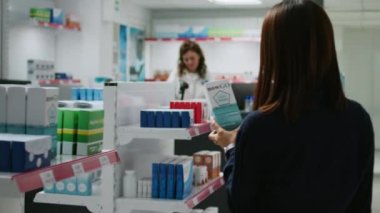 Sağlık danışmanı eczane tezgahındaki Asyalı kadına tıbbi tedavi ve vitaminleri açıklayan ilaç paketini gösteriyor. Çeşitli insanlar tıptan bahsediyor..