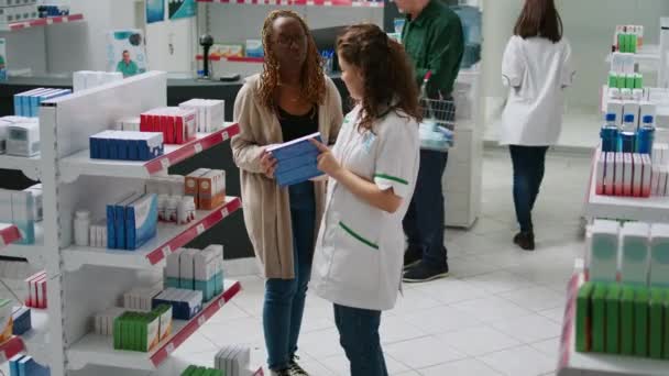 Жіночий Фармацевт Допомагає Афроамериканському Клієнту Вибирати Ліки Пояснюючи Листівки Добавок — стокове відео