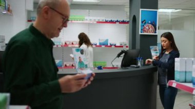 Kardiyoloji hapı alan ve eczane tezgahında akıllı bir şekilde ödeyen bir kadın. Reçeteli tedavi için NFC kullanıyor. Eczaneden sağlık ürünleri ve takviyeler satın almak.