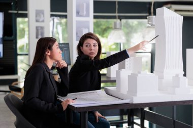 Proje taslağında çalışan kadınlar, mimarlık ofisinde 3D baskı modelini tartışırlar. Ortak çalışma alanı ve inşaat endüstrisinde mimari prototipi işaret eden mimar.